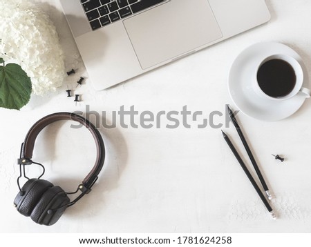 Home office desk workspace with laptop, black coffee in cup, pencils, white hydrangea and headphones on a white background. Flat lay, top view girl work business concept.