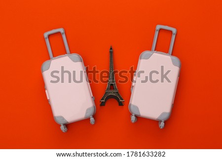 Two toy travel luggage, eiffel tower figurine on orange background. Travel planning. Top view. Flat lay