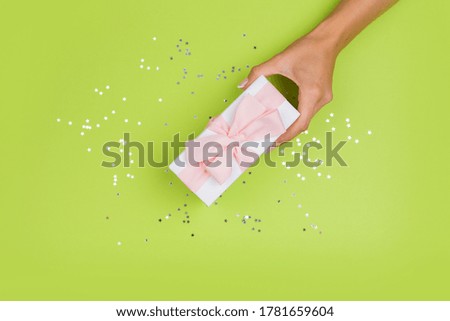 Women hands holding a gift or gift box decorated with confetti on a green table top view. 