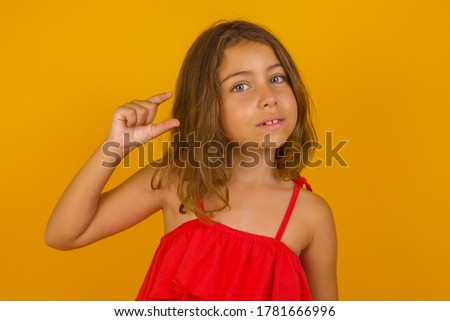 Blonde European kid over isolated background gesturing with hand showing small size, measure symbol. Smiling looking at the camera. Measuring concept.