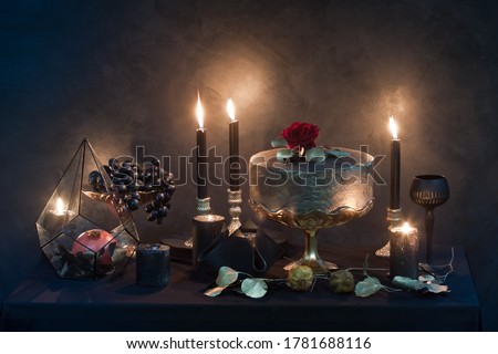 mysterious looking still life with handmade figure of cake, burning candles, dried rose and pomegranate, craft art of wedding decoration details