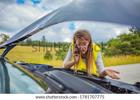 Young woman with broken car calling for help. Worried woman talking on the phone near broken car. White girl model standing near the broken car calling for auto repair service