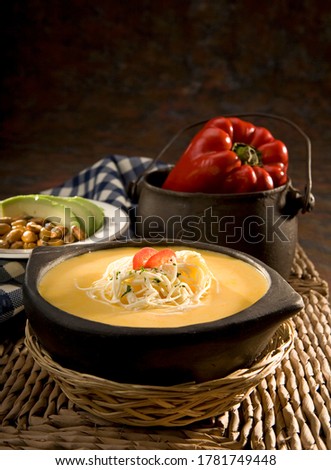Famous traditional Ecuadorian soup called "Locro de Papa", or potato soup, presented in a ceramic pot in which it was cooked. Garnished with fresh string cheese, parsley and tomato slices.  Royalty-Free Stock Photo #1781749448