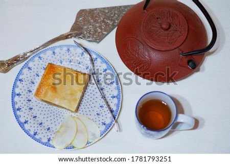 Cenital tea scene with a piece of apple pie in a porcelain dish, a teapot and a cup of tea with a white background 