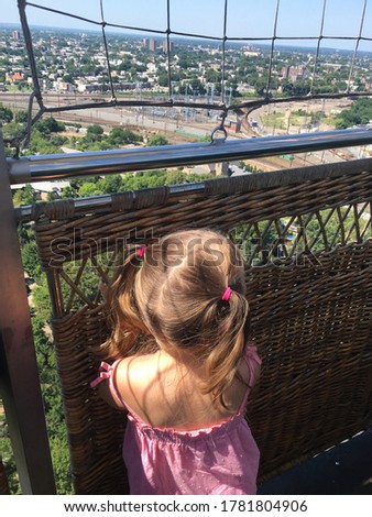 Little girl with blonde pig tails and pink shirt gazing out basket of balloon at Philadelphia sky line