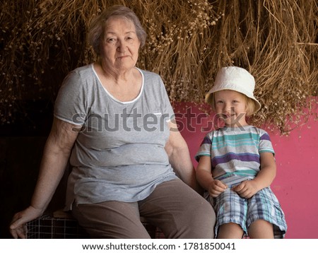 elderly woman withblond boy on background with dried chamomile flowers. grandson loves to spend time with his grandmother
