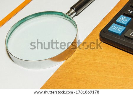 A loupe is on the table, a magnifying glass is lying with a white pencil on a white sheet.