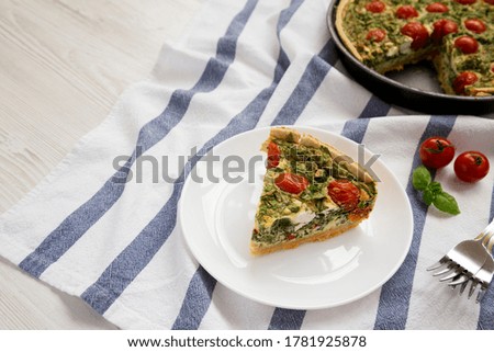 A Piece of Homemade Spinach Quiche on a white plate, side view. Copy space.