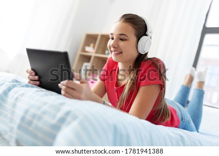 children, technology and communication concept - smiling teenage girl in headphones listening to music on tablet computer at home