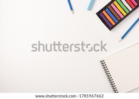 Colored wax crayons, sketchbook isolated on white background. Colorful chalk. Flat lay, top view, copy space.