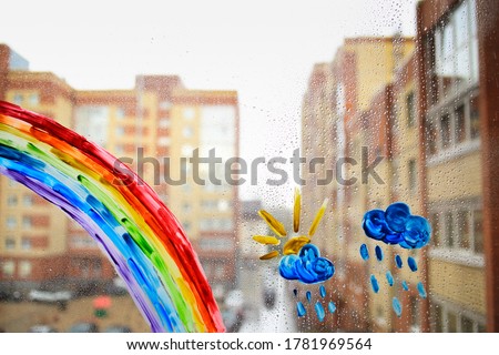 Rainbow.Cloud on the window.Raindrops on the glass. Children's drawing on the window with paints on the background of the city.The sun comes out from behind the clouds.Draw using colors