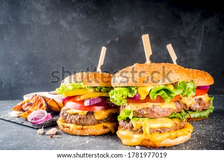 Tasty grilled homemade cheeseburgers with beef, tomato, cheese, tomato and lettuce. On dark grey background, with sauces. Top view copy space