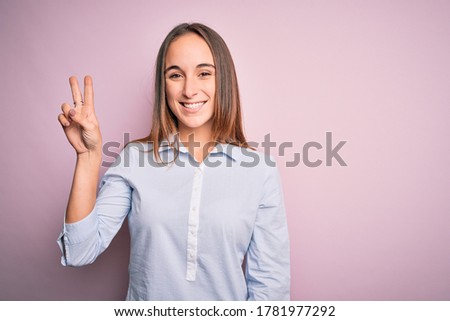 Young beautiful businesswoman wearing elegant shirt standing over isolated pink background showing and pointing up with fingers number two while smiling confident and happy.