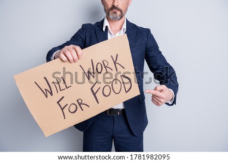 Cropped photo of serious poor homeless dismissed man suffer financial crisis lost work job hold placard search work for food exchange direct finger card wear suit isolated grey background