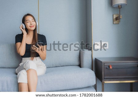 Portrait beautiful young asian woman use smart mobile phone with headphone for listen music on sofa in living room area