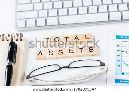 Total assets concept with letters on cubes. Still life of office workplace with supplies. Flat lay grey surface with computer keyboard and notepad. Capital investment and financial analytics.
