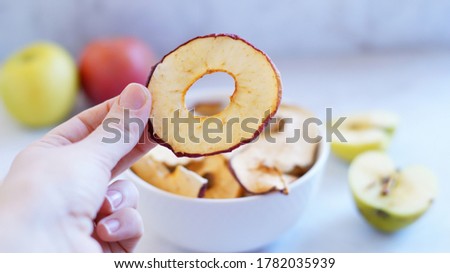 Apple chips in hand on the background of a plate of chips