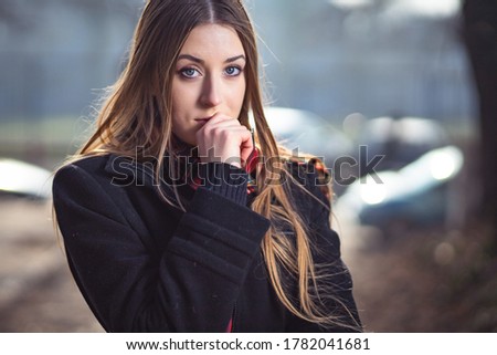 Outdoor portrait photo of cute blonde girl in black jacket and red scarf looking worried