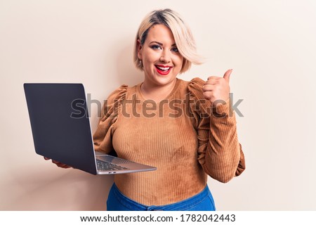 Young beautiful blonde plus size woman working using laptop over isolated white background smiling happy and positive, thumb up doing excellent and approval sign