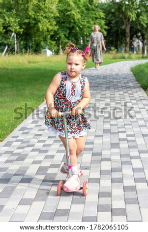 little girl rides a scooter on the sidewalk in the park on a summer sunny day