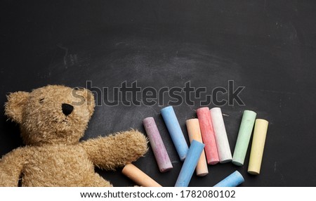 brown teddy bear and colorful crayons on black chalk board, back to school