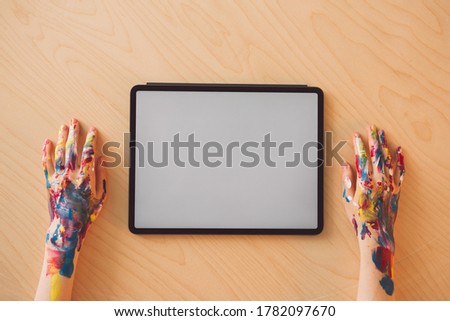 Close up view of designer workplace with blank screen tablet and painter's hands in paints, top view