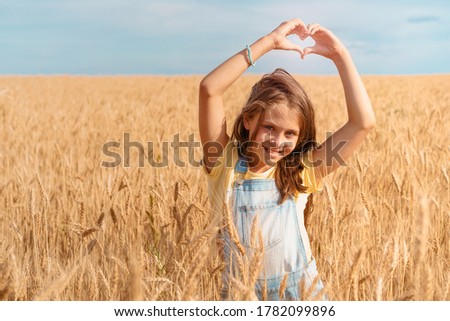 Cute little girl in a wheat field shows a heart made of fingers, a place for text