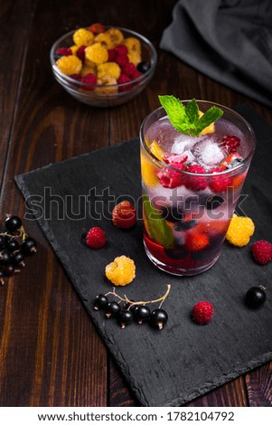Berry lemonade in a transparent glass on a dark background.