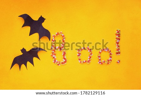 Halloween holiday decorations of two paper bats flying over an orange background with candy corn text spelling out the word boo. Top view. 