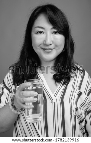 Portrait of mature beautiful Asian businesswoman with glass of water