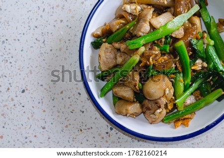 Picture of Stir-fried pork noodles with soy sauce and Kale, straw mushroom, served in a plate, and put on the marble table.