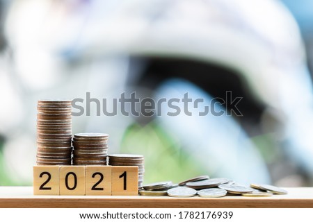There are coins putting on the wooden table like a growing graph. With text 2021, On green blurry bokeh background. And copy space. Saving money and finance concept.