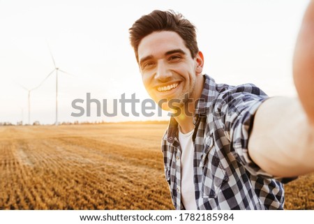 Happy man taking selfie against the industrial landscape with wind turbines