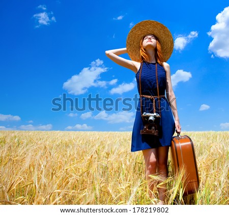 Redhead girl with suitcase at spring wheat field. Royalty-Free Stock Photo #178219802