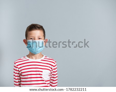 Portrait of a 7 year old boy covering his face with a face mask to protect himself from COVID-19, isolated on gray background, with copy space Royalty-Free Stock Photo #1782232211