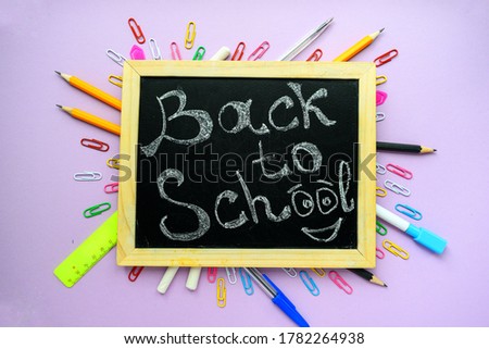 Back to school text on a black school board with a wooden frame on a purple background and stationery.