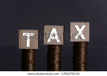 Tax increasing conceptual image. Wooden blocks form word TAX on stacked coins. Financial concept