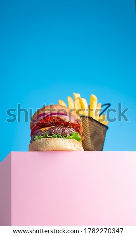Fresh juicy beef hamburger and fried french fries placed on the pink stand and blue background. Copy space for text, trendy hero view