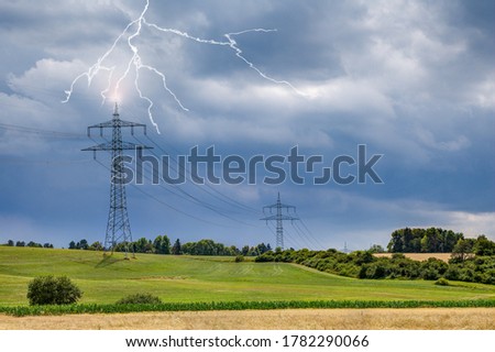 On the sultry, hot summer day, looming storm clouds appear in the sky on the upper Au area near the small town of Trossingen and lightning strikes the high-voltage pylon. Royalty-Free Stock Photo #1782290066