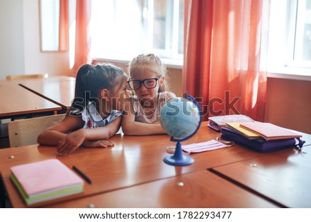 Two schoolgirls sit at a school desk and discuss the purpose of the lesson.