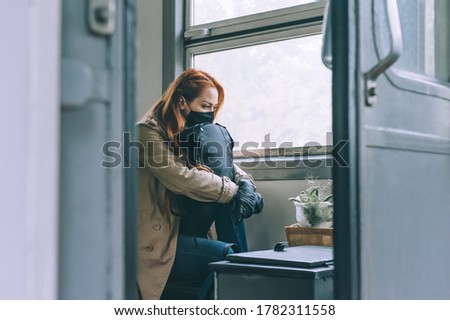 A sad girl, in a medical mask, sits on a train near the window