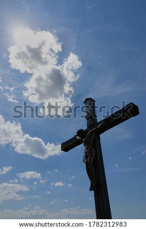 Jesus figure ( cruci fixus ) can be seen as a silhouette on a brown wooden cross. Motif runs obliquely into the picture. Blue sky with white clouds. Germany.