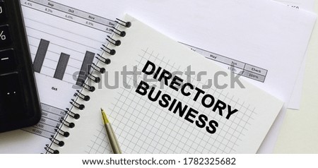 Text DIRECTORY BUSINESS on the page of a notepad lying on financial charts on the office desk. Near the calculator. Business concept.