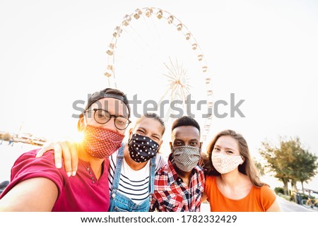 Multiracial milenial students taking selfie protected by face masks - New normal travel concept with young people having safe fun together at ferris wheel - Bright sunshine filter with tilted angle Royalty-Free Stock Photo #1782332429