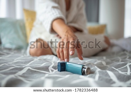 Girl suffering asthma attack reaching inhaler sitting on a bed in the bedroom at home. Woman Hand Reaching Inhaler Because She Suffering From Asthma Attack  Royalty-Free Stock Photo #1782336488