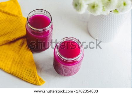Dragon fruit Juice in a jar, yellow napkin, some plants, and white background.