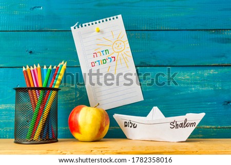 inscription in Hebrew Back to school on a sheet of paper with pencils and paper boat.