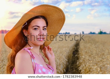 Portrait of smiling young long-haired Ukrainian woman in a straw hat in a wheat field at dawn