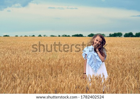 Beautiful tender girl with long blond hair in a white dress admires a field of wheat