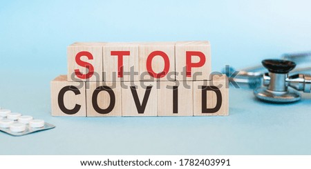 text STOP COVID-19 on wooden cubes on blue background with tablets and stethoscope. Stop the global coronavirus pandemic.